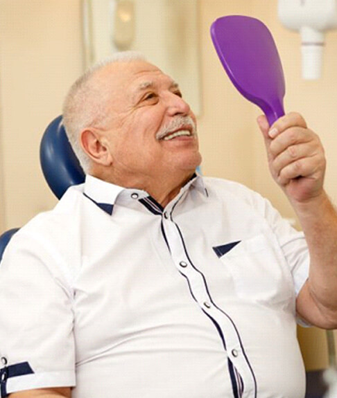 senior dental patient holding mirror and smiling