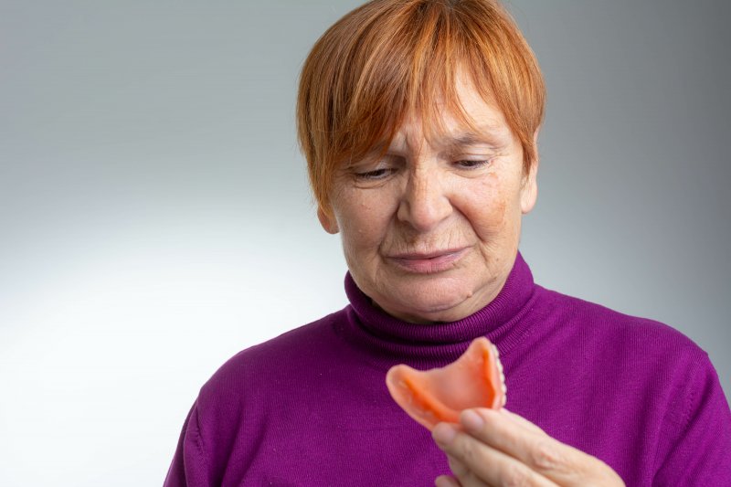 An unhappy senior woman holding a denture